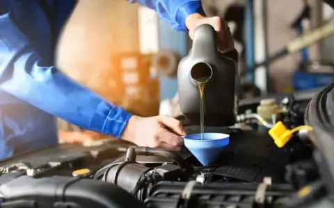 Mechanik w niebieskim kombinezonie nalewa olej do silnika przez lejek. Szybka wymiana oleju to klucz do sprawnego działania auta.
