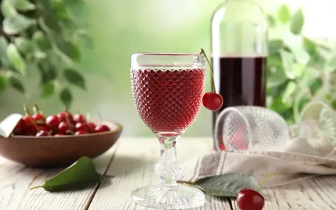 Szklanka z czerwonym winem, wiśnie i butelka. Idealny przepis na wino czerwone z wiśni.