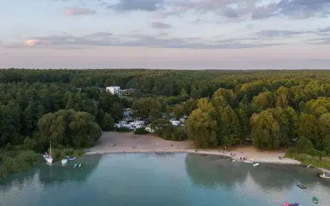 Widok na kemping nad najczystszym jeziorem w Polsce. Woda jest turkusowa, a brzeg piaszczysty. W oddali las.