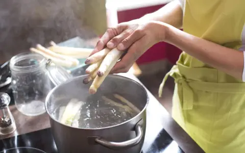Frischer weißer Spargel wird in kochendes Wasser gegeben. Die Frage, wie lange muss Spargel kochen, beschäftigt viele Hobbyköche.