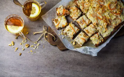 En skiva vegansk morotskaka med glasyr och nötter, serverad med två koppar te med citron.