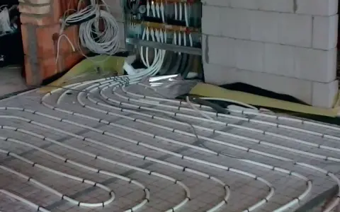 Instalacja ogrzewania podłogowego. Rury ułożone na siatce, podłączone do rozdzielacza. To rozwiązanie obniża koszt ogrzewania.