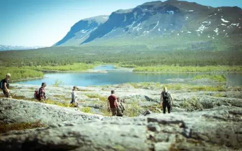 Vandring i **Laponia nationalpark** med fjäll, sjö och skog. En grupp vandrare njuter av den storslagna naturen.