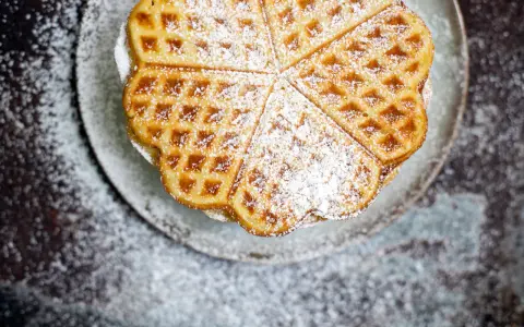 Herzförmige Waffeln, bestäubt mit Puderzucker, auf einem Teller. Ein köstliches Rezept für süße Momente.