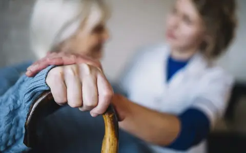 Opiekunka wspiera starszą panią, która trzyma laskę. Zastanawiasz się, ile kosztuje opiekunka z mops?