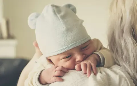 Nyfödd bebis med mössa med öron, tryggt vilande mot en axel. En perfekt baby gåva.