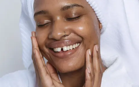 Visage radieux d'une femme souriante, peau hydratée après l'utilisation de rétinol. Elle porte une serviette sur la tête et un peignoir blanc.