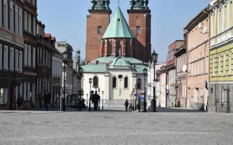 Spacer po brukowanym rynku Gniezna, z katedrą w tle. Kolorowe kamienice po bokach tworzą urokliwą atmosferę.