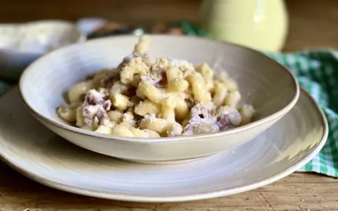 Piatto di pasta con prosciutto crudo, formaggio grattugiato e una salsa cremosa. Un classico confortante.