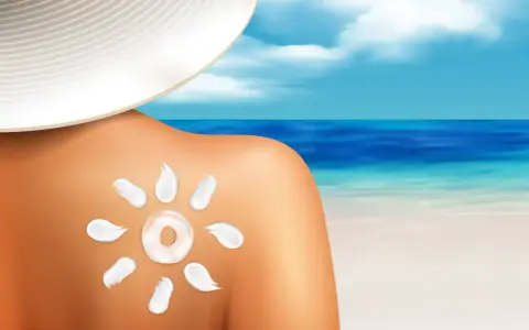 Słońce na plecach po opalaniu. Krem przeciwsłoneczny w kształcie słońca na skórze, plaża i morze w tle.