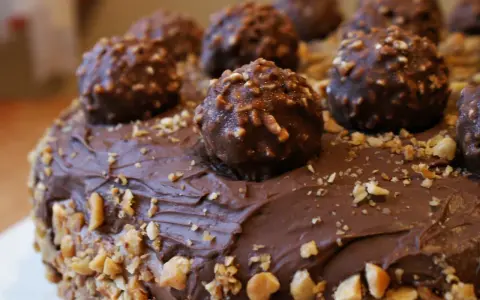 Pyszny tort ferrero rocher, obficie udekorowany czekoladowymi kulkami i posypany orzechami.