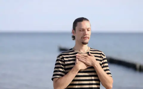 Mann mit geschlossenen Augen und Händen auf der Brust, genießt die frische Meeresluft. Eine asthma kur am meer kann Wunder wirken.