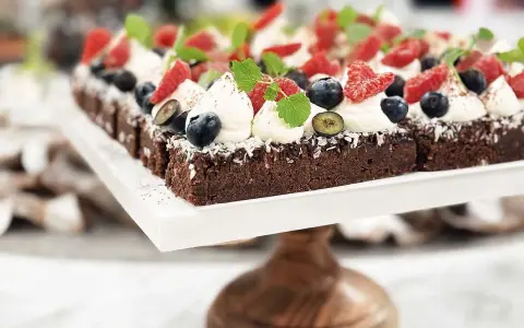 En rad läckra bitar kladdkaka med fudge, toppade med vispad grädde, färska bär och mynta.