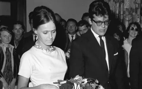 Elżbieta Chwalibóg z bukietem kwiatów u boku męża w garniturze, otoczeni ludźmi.