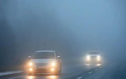 Dwa samochody jadące we mgle, z włączonymi światłami. Warto pamiętać o odpowiednich światłach do jazdy dziennej w takich warunkach.