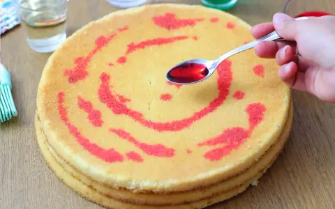 Un cucchiaino di sciroppo rosso viene versato su un pan di spagna decorato con un motivo a spirale. La bagna per pan di spagna renderà la torta più umida e saporita.