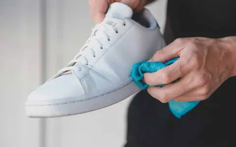 Manos limpiando zapatillas blancas de tela con un paño azul.