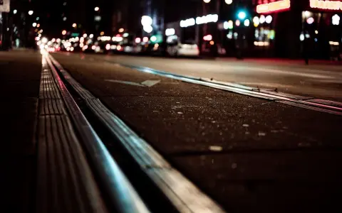 Torowisko tramwajowe w nocy, światła miasta rozmyte, jakby w ślepocie zmierzchowej.