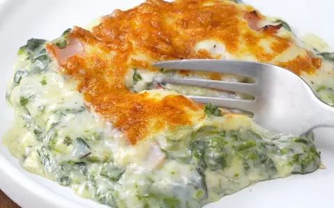 Deliciosa lasaña de espinacas cremosa, gratinada y lista para disfrutar. Un tenedor se hunde en esta maravilla.