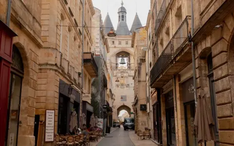 A charming street in Bordeaux leads to the iconic Grosse Cloche bell tower. Cafes and shops line the cobblestone path, making you wonder, is Bordeaux worth visiting? Absolutely!