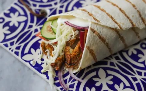 Pyszny kebab zawinięty w tortillę, z soczystym mięsem, chrupiącą sałatą, pomidorem, ogórkiem i czerwoną cebulą. Idealny przepis na szybki obiad.