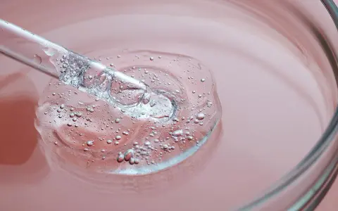 Goccia di siero trasparente con bollicine, su sfondo rosa. Un tocco di vitamina B3 per il viso.