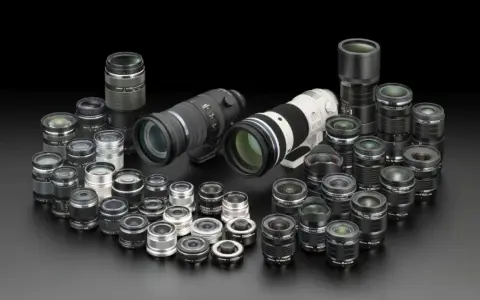 Collezione di obiettivi fotografici di varie dimensioni, dai teleobiettivi ai grandangolari, disposti su sfondo nero. Un vero tesoro per ogni appassionato di termini fotografici.