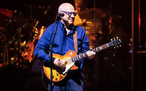 Mark Knopfler na scenie, grając na gitarze Gibson Les Paul. Jego charakterystyczne utwory brzmią w tej chwili na żywo.