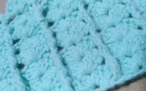 Textura de un tejido a crochet en tono azul claro. Se aprecian los detalles de un punto fantasía, creando un patrón con relieve y pequeños huecos.