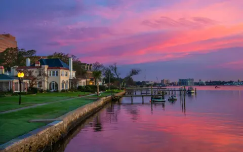 Beautiful waterfront homes and boats reflect a vibrant pink and purple sunset, perfect for weekend trips from Richmond, VA.
