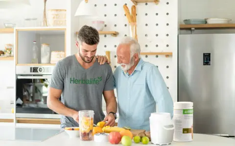 Två män i ett kök förbereder en smoothie med frukt. En burk med proteinpulver står bredvid, perfekt för att veta hur mycket protein per dag du behöver.