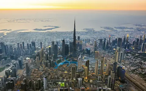 Luftaufnahme von Dubai bei Sonnenuntergang. Der Burj Khalifa ragt empor, umgeben von Wolkenkratzern und den künstlichen Inseln. Ein Blick auf die Dubai Besonderheiten.