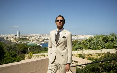 A man in a light tan suit, tie, and sunglasses offers inspiration for what to wear to a communion as a guest male.