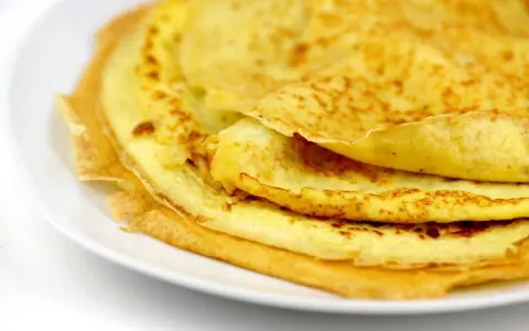 Ein Stapel goldbrauner Eierkuchen auf einem weißen Teller. Perfekt für ein schnelles und einfaches Eierkuchen Rezept.