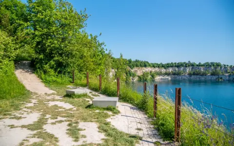 Ścieżka spacerowa nad turkusową wodą w kamieniołomie. Zakrzówek trasa zachęca do odpoczynku na ławkach wśród zieleni.