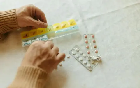 Dłonie układają tabletki w organizerze. Obok leżą blistry. Gdzie kupić tabletki antykoncepcyjne bez recepty?