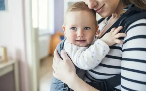Uśmiechnięte dziecko w nosidle od urodzenia, przytulone do mamy.