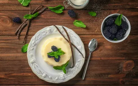 Budino fatto in casa alla vaniglia, guarnito con more fresche e menta. Ingredienti genuini per un dolce delizioso.