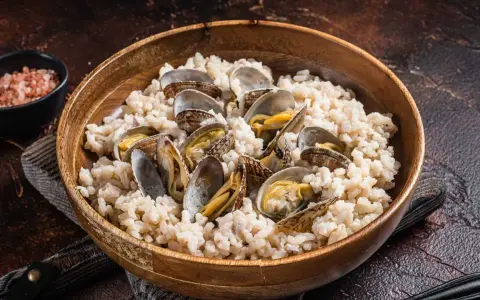 Un delicioso arroz con almejas, servido en un cuenco de madera. Las almejas, abiertas y jugosas, se mezclan con el arroz cremoso.