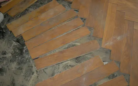 Drewniana podłoga w jodełkę, częściowo rozebrana. Widać luźne deseczki i pył. Subit co to?