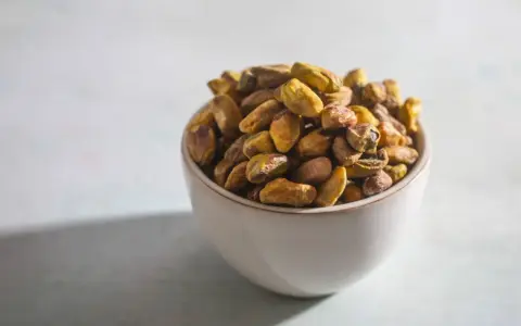 Misternie ułożone pistacje w miseczce. Czy pistacja to orzech? Botanicznie to pestkowiec, ale kulinarnie często traktowany jak orzech.