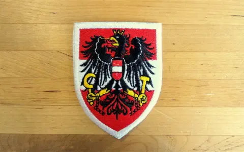 Naszywka z godłem Austrii: czarny orzeł z tarczą w biało-czerwone pasy, trzymający sierp i młot.