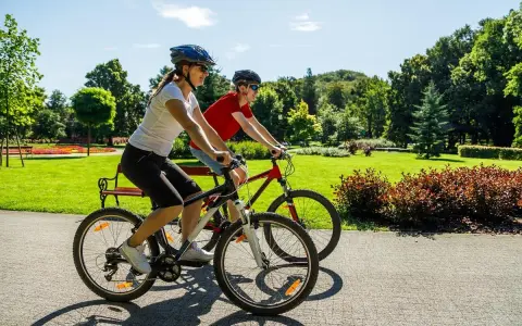 Dwie osoby na rowerach cieszą się piękną pogodą w parku. To pokazuje, co daje jazda na rowerze: aktywność, relaks i kontakt z naturą.