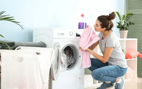 Junge Frau lädt Wäsche in die Waschmaschine. Sie hält ein rosa gestreiftes Kleidungsstück, bereit zum leinen waschen.