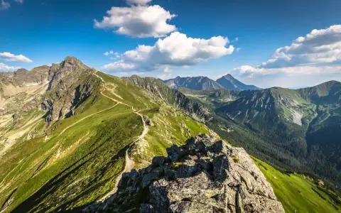 Malownicza trasa pieszo na Kasprowy Wierch. Kręta ścieżka wije się pośród zielonych zboczy Tatr, pod błękitnym niebem z chmurami.
