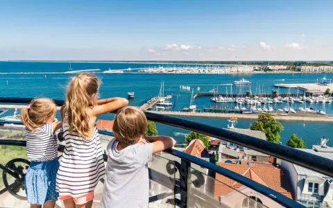 Drei Kinder blicken auf einen belebten Hafen mit vielen Segelbooten. Ein schöner Tag für Veranstaltungen MV mit Kindern.