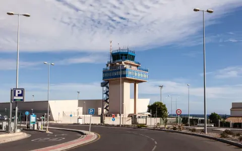 Kontrollturm am Almeria Airport mit Parkplatzschildern und Straßenbeleuchtung unter blauem Himmel.
