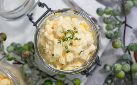 Cremiger Kartoffelsalat mit Fleischsalat, garniert mit frischen Kräutern, in einem Glas serviert.