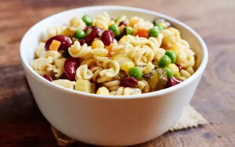 Una ciotola di pasta fredda con fagioli rossi, piselli, mais e cetriolini. Un piatto estivo perfetto.