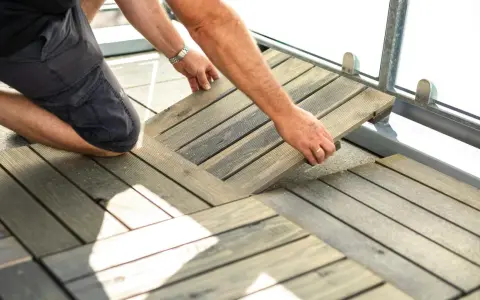 Mann legt Holzfliesen für den dachterrasse gestalten boden. Die Holzoptik passt gut zu modernen Außenbereichen.